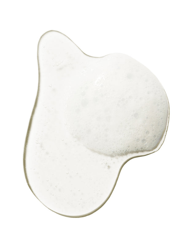 A clear swatch of Burdock and Neem shampoo forms an irregular pool on white. Fine white foam and small bubbles collect across its centre and along one side.