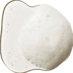 A translucent swatch of 100% Pure Kelp & Mint Volumising Shampoo, forming an uneven puddle with white froth and small bubbles through the centre.
