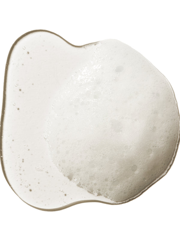 A translucent swatch of 100% Pure Kelp & Mint Volumising Shampoo, forming an uneven puddle with white froth and small bubbles through the centre.
