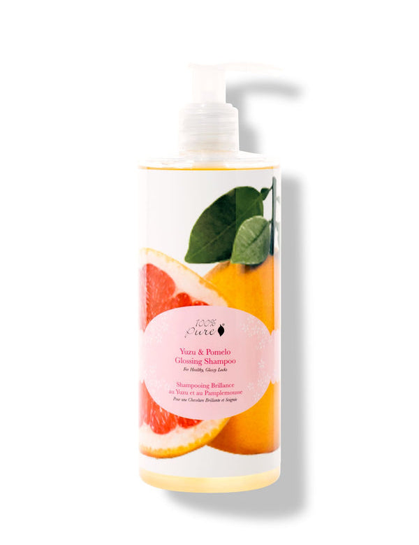100% Pure Yuzu & Pomelo Glossing Shampoo in a white pump bottle, with a large pink citrus slice, yellow fruit, green leaves and a round pink label on the front.