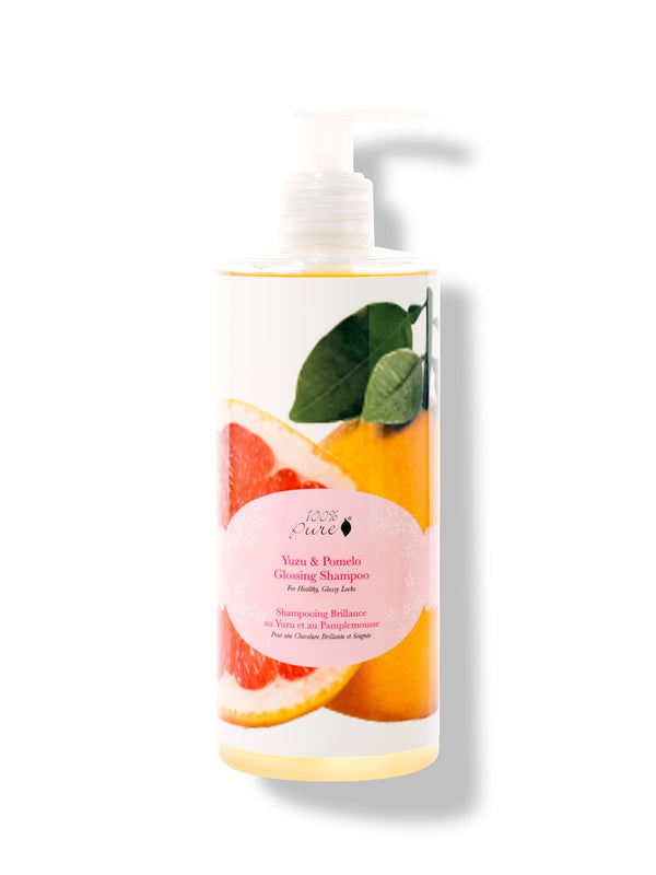 100% Pure Yuzu & Pomelo Glossing Shampoo in a white pump bottle, with a large pink citrus slice, yellow fruit, green leaves and a round pink label on the front.