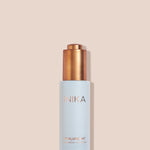 Pale blue INIKA Hyaluronic Hydration Complex bottle standing upright with its gold pump exposed on a beige background, casting a narrow shadow to the right.