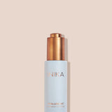 Pale blue INIKA Hyaluronic Hydration Complex bottle standing upright with its gold pump exposed on a beige background, casting a narrow shadow to the right.