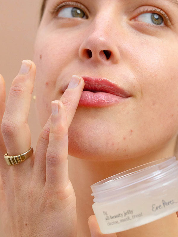 Woman applying Ere Perez Fig All-Beauty Jelly to her lips with the open jar in the foreground