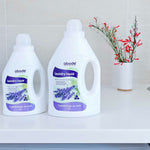 Two bottles of Abode Laundry Liquid Lavender and Mint on a washing machine with fresh flowers