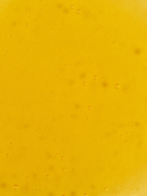 Close-up of golden-yellow Noni Radiant Eye Oil with small bubbles scattered through its smooth, translucent surface.