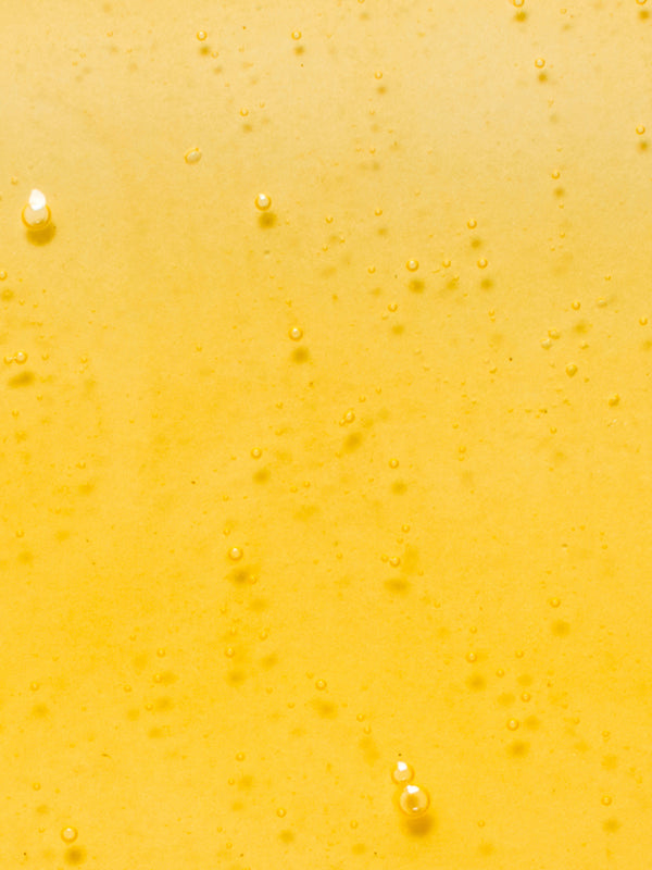 Close-up of golden-yellow Kakadu Plum Vitamin C Serum dotted with tiny bubbles and a few larger round air bubbles.
