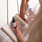Woman relaxing with a book holding the Mukti Vital A Vitamin Booster bottle