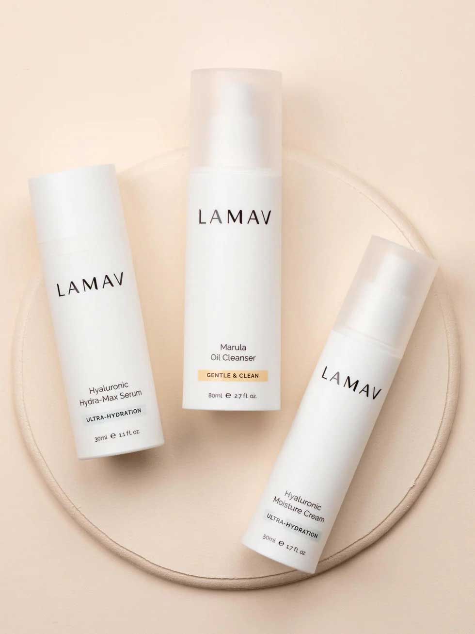 Three white bottles of LAMAV Hydration Skin Discovery Pack (3 Pack), featuring hyaluronic acid-powered formulas for ultimate hydration, arranged on a beige circular surface against a neutral background.