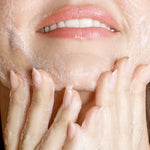 Model lathering KORA Organics Turmeric Glow Foaming Cleanser on her cheek