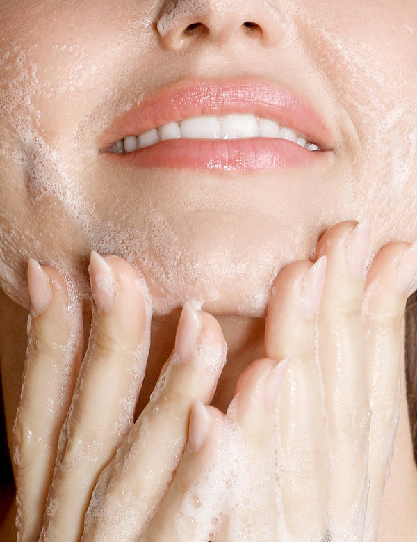 Model lathering KORA Organics Turmeric Glow Foaming Cleanser on her cheek