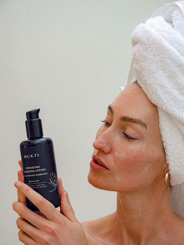Woman in a towel turban reading the Mukti Hydrating Cleansing Lotion label