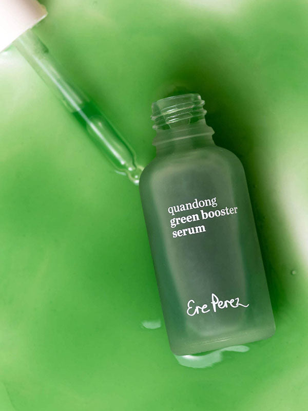 Ere Perez Quandong Green Booster Serum pouring from an open green glass bottle with the dropper alongside