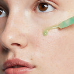 Close-up of Ere Perez Quandong Green Booster Serum dropped onto a woman's cheek from the dropper