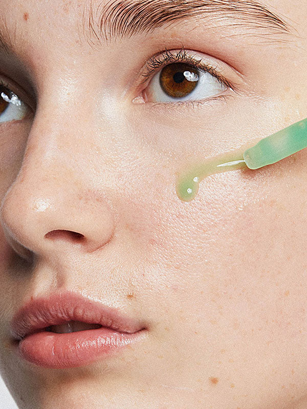 Close-up of Ere Perez Quandong Green Booster Serum dropped onto a woman's cheek from the dropper