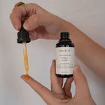 Hands drawing golden serum from the Mukti Vital A Vitamin Booster bottle with the dropper