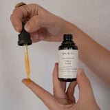 Hands drawing golden serum from the Mukti Vital A Vitamin Booster bottle with the dropper