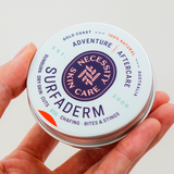 Necessity Surfaderm tin held in hand
