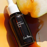 Ere Perez Guava Gradual Tan amber dropper bottle lying beside fresh guava in a pool of tan serum