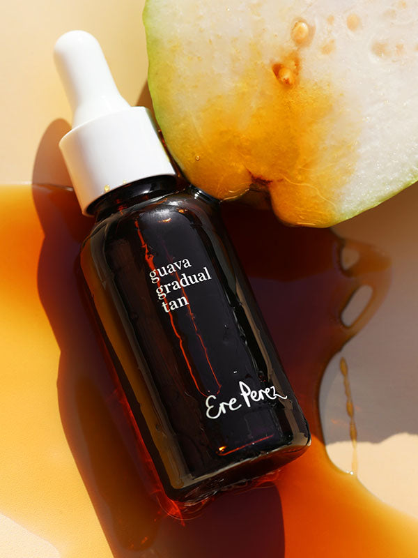 Ere Perez Guava Gradual Tan amber dropper bottle lying beside fresh guava in a pool of tan serum