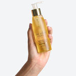 Hand holding a bottle of The Jojoba Company Jojoba Activating Cleansing Oil