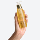 Hand holding a bottle of The Jojoba Company Jojoba Activating Cleansing Oil