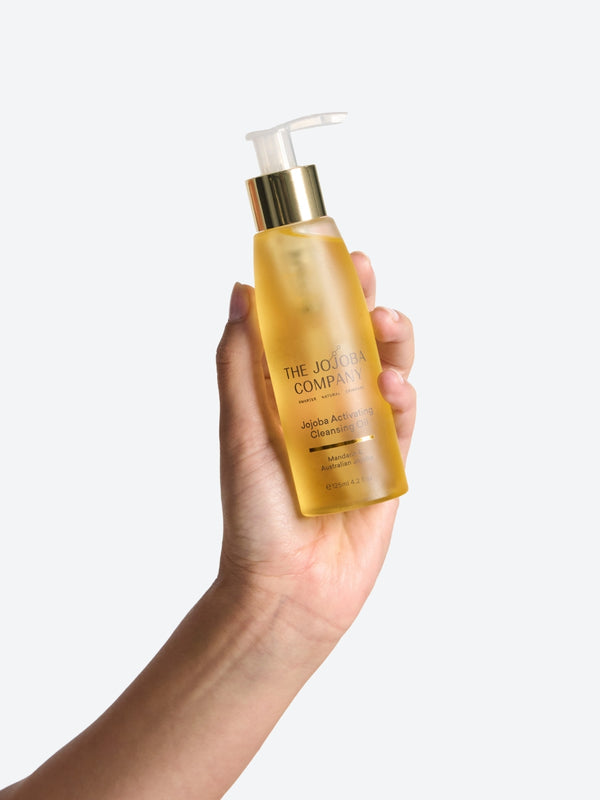 Hand holding a bottle of The Jojoba Company Jojoba Activating Cleansing Oil