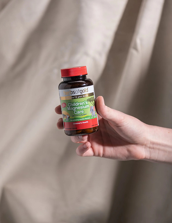 Hand holding the Herbs of Gold Children's Magnesium Care bottle