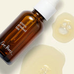 Ere Perez Guava Gradual Tan bottle standing beside droplets of the golden tanning serum