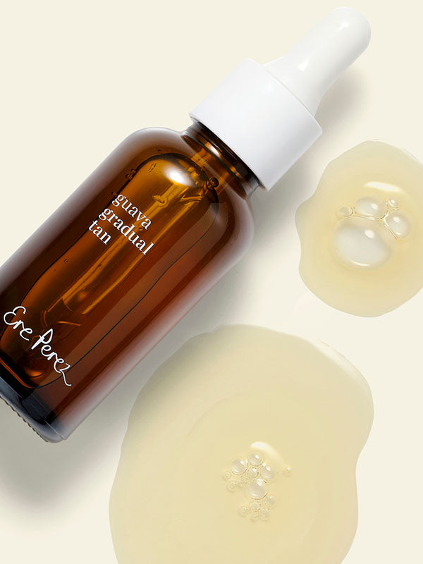 Ere Perez Guava Gradual Tan bottle standing beside droplets of the golden tanning serum