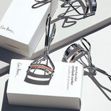 Two Ere Perez Spectacular Eyelash Curlers with their boxes on a white background