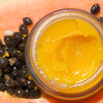 Ere Perez Papaya SOS Marmalade open jar of golden balm resting on a fresh papaya with seeds