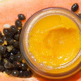 Ere Perez Papaya SOS Marmalade open jar of golden balm resting on a fresh papaya with seeds