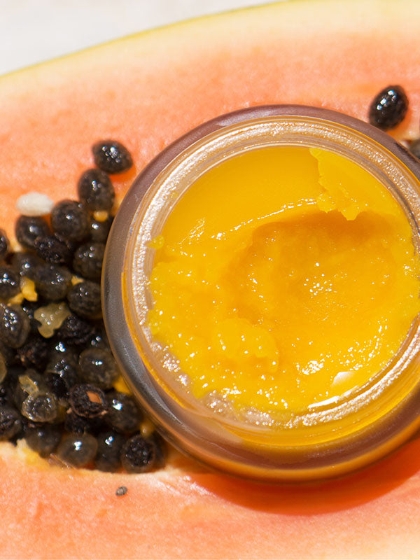 Ere Perez Papaya SOS Marmalade open jar of golden balm resting on a fresh papaya with seeds