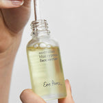 Hands lifting the dropper from an open bottle of Ere Perez Australian Blue Cypress Face Nectar