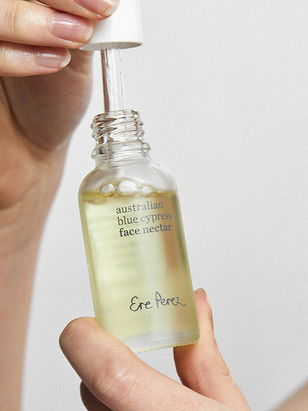 Hands lifting the dropper from an open bottle of Ere Perez Australian Blue Cypress Face Nectar
