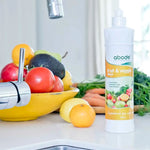 Abode Fruit and Vegetable Wash bottle at the kitchen sink beside a bowl of fresh produce