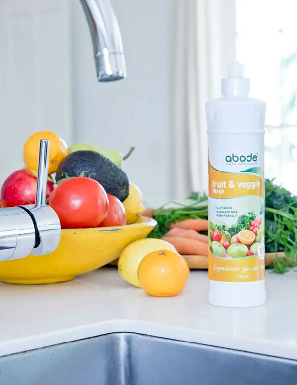 Abode Fruit and Vegetable Wash bottle at the kitchen sink beside a bowl of fresh produce