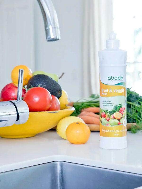 Abode Fruit and Vegetable Wash bottle at the kitchen sink beside a bowl of fresh produce