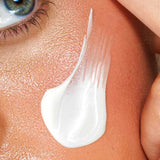 A close-up of a person’s smooth skin and blue eye, with a streak of Avocado Zinc SPF50 Natural Physical Face Sunscreen 100ml on their cheek as a finger gently touches the skin near the temple.