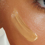 A close-up of a tan cheek as Avocado Zinc SPF 50 Natural Tinted Moisturiser 50ml in Light-Medium is applied, alongside a white tube, highlighting this facial sunscreen's natural sun protection.