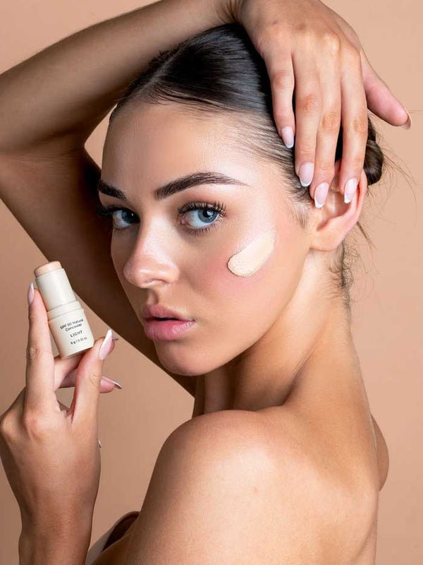 Model applying Avocado Zinc SPF50 Natural Concealer in Light to her cheek.
