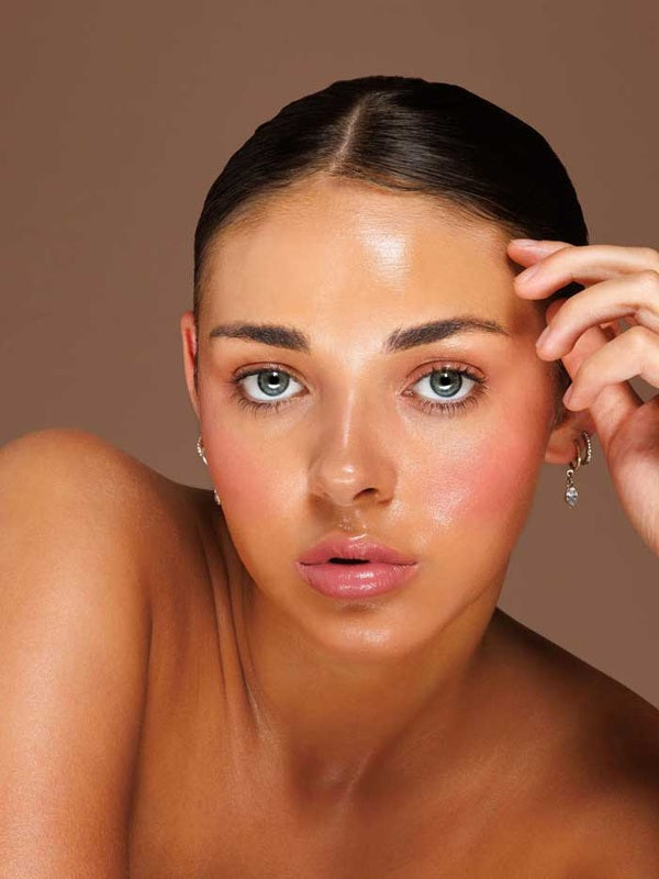 Model wearing Avocado Zinc SPF50 Natural Lip & Cheek Tint in Berry and holding the tint beside her face.