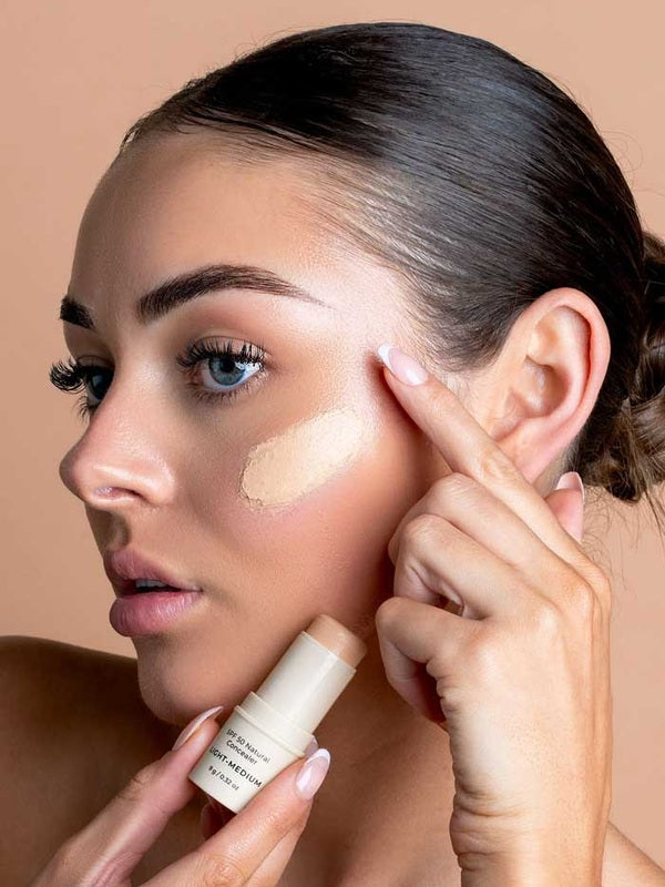 Model blending Avocado Zinc SPF50 Natural Concealer in Light-Medium beneath her eye.
