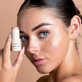 Model holding Avocado Zinc SPF50 Natural Concealer in Medium-Dark beside the cheek swatch.