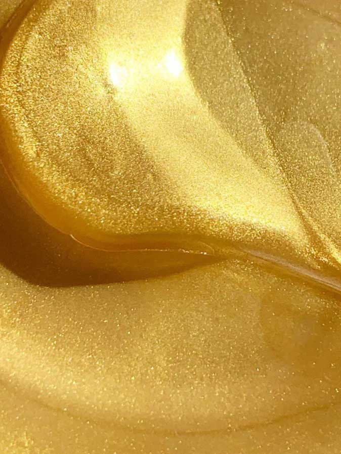 Close-up of a shiny, swirling golden liquid with a smooth texture and glimmering highlights, reminiscent of the luminous appearance of Acure Radically Rejuvenating Under Eye Hydrogels 4g.