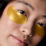 Model wearing gold Acure Radically Rejuvenating Under Eye Hydrogels beneath both eyes.