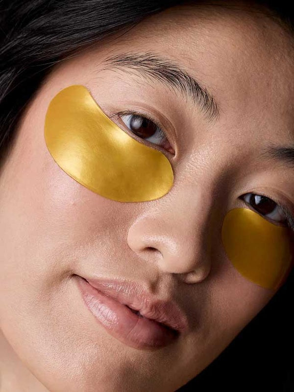Model wearing gold Acure Radically Rejuvenating Under Eye Hydrogels beneath both eyes.