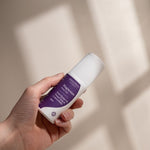 Amazing You Sleep Magnesium Gel 60ml roll-on held in one hand, with its purple label and white cap visible against a sunlit wall.