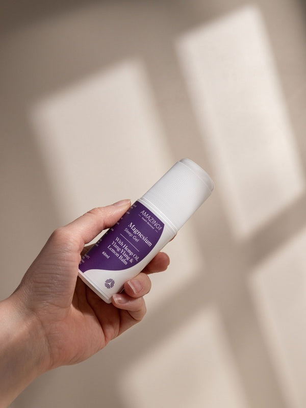 Amazing You Sleep Magnesium Gel 60ml roll-on held in one hand, with its purple label and white cap visible against a sunlit wall.